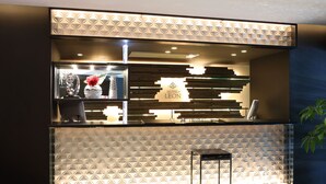 A modern hotel reception area with a geometric patterned wall, a reception desk, and a staircase leading to the upper floor. - Hotel Leon Hamamatsu (Hamamatsu)