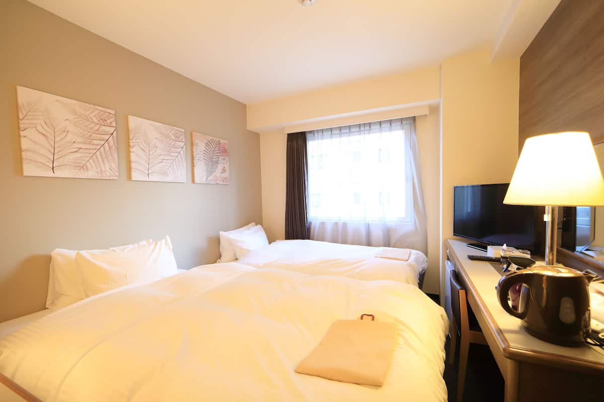 A hotel room with a large bed, a desk with a television, and a window with curtains.