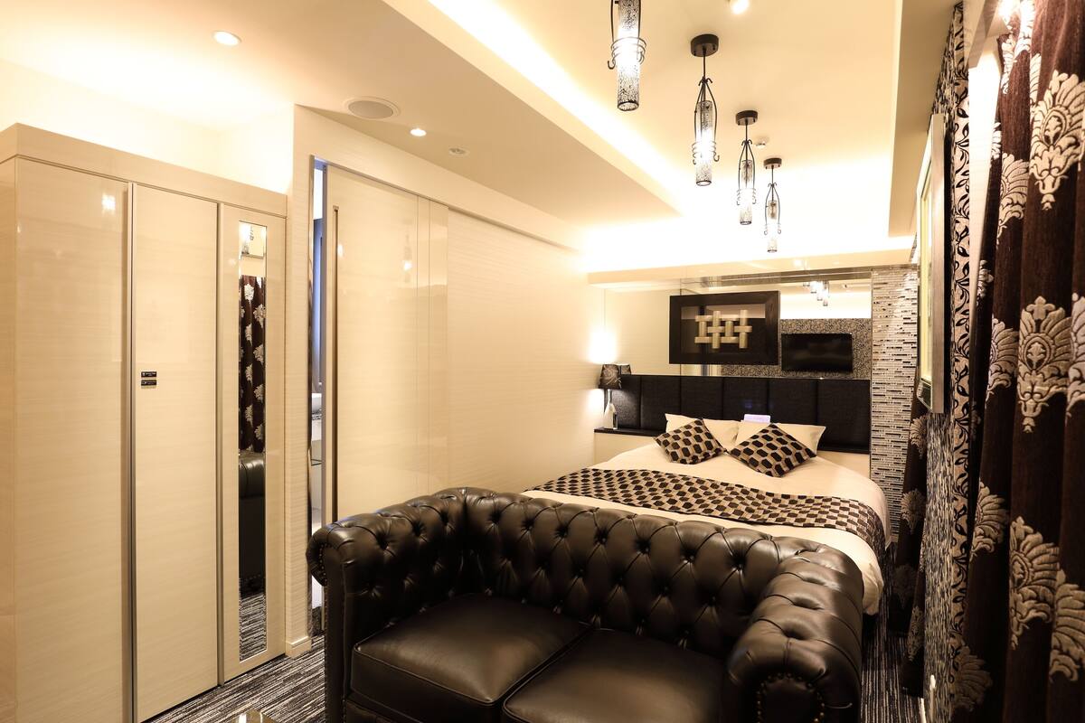 A modern bedroom with a large bed, a leather sofa, and a walk-in closet.