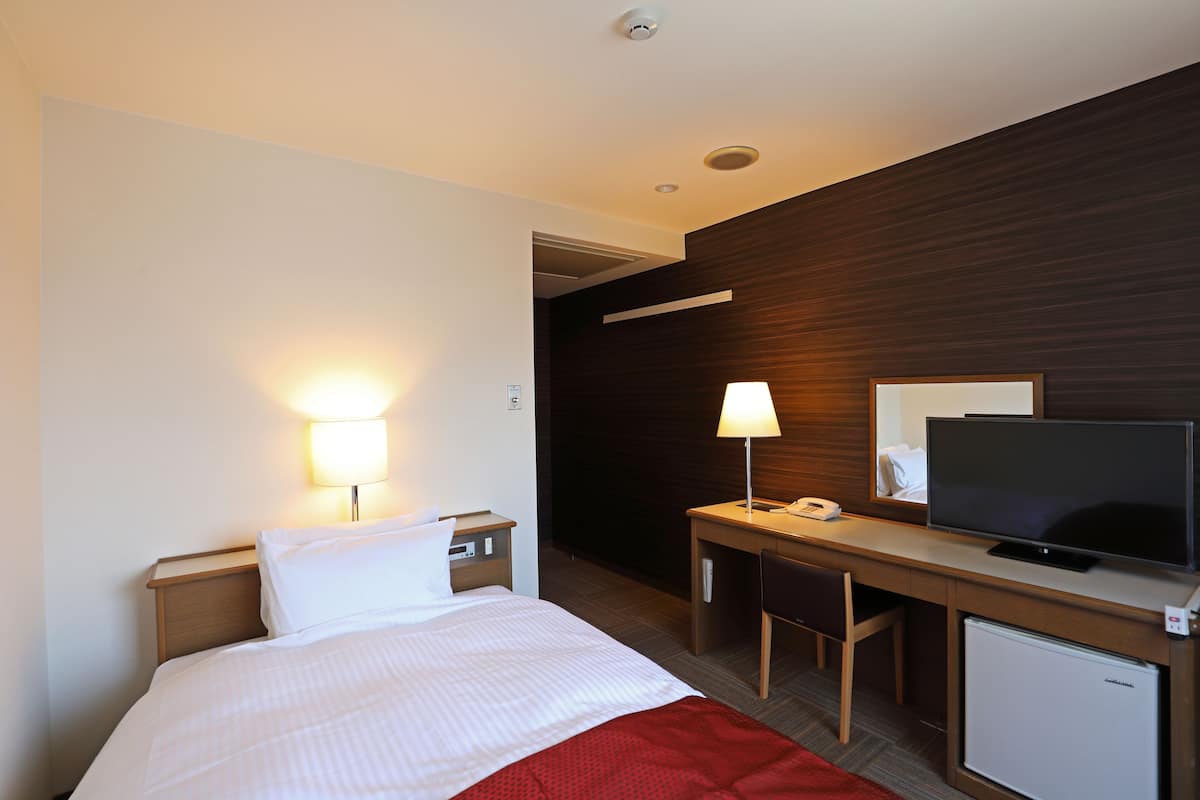 A hotel room with a bed, bedside lamps, a desk with a chair, a television, and a mini-fridge.