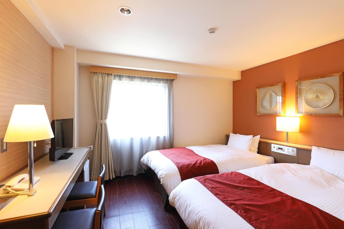 A hotel room with two beds, a desk with a lamp, a TV, and a telephone.