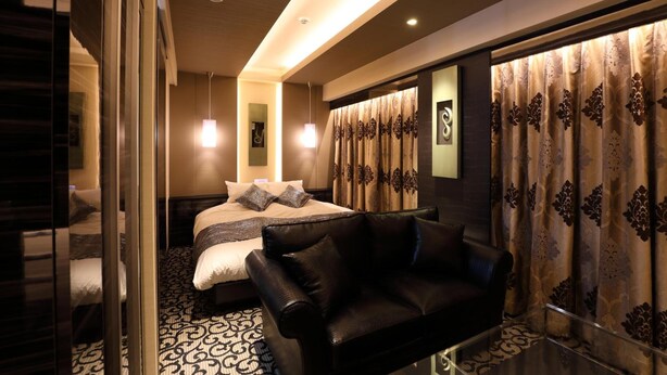 A modern hotel room with a bed, a black leather sofa, patterned curtains, and a glass partition. - Hotel Leon Hamamatsu (Hamamatsu)