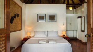 Cama bem arrumada com lençóis brancos e duas luminárias de cabeceira, moldura de porta de madeira e piso de azulejos.