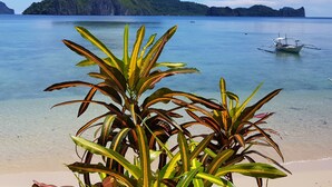 Uma praia tropical com águas cristalinas, um barco pequeno e vegetação exuberante em primeiro plano.