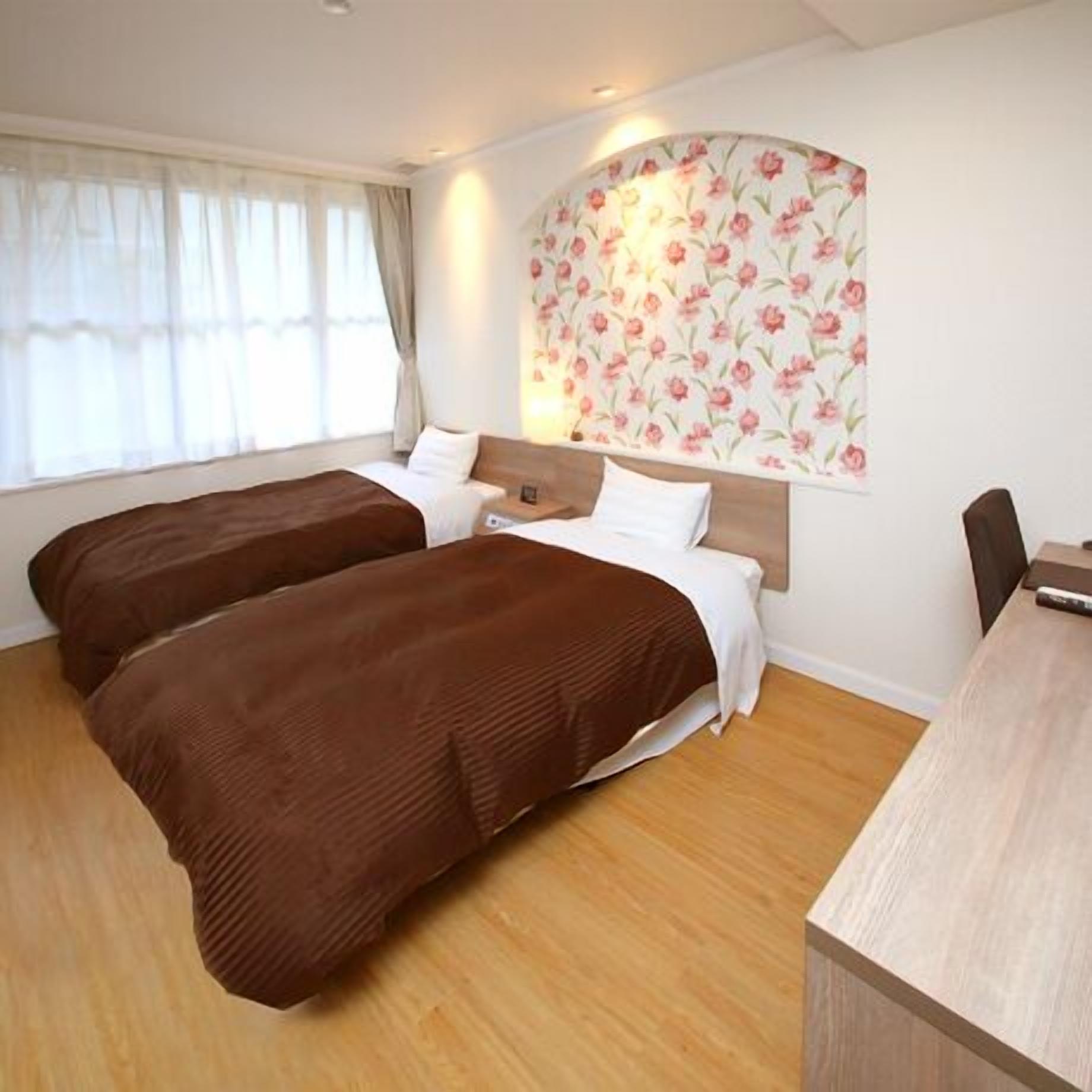 A hotel room with two beds, a desk, and a floral wallpaper.