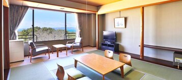 Habitación con esteras de tatami, una mesa de madera, sillas, un televisor y vistas al exterior.