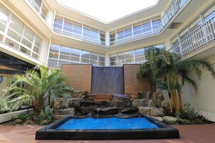 Un atrio de varios niveles con una cascada central, rodeado de plantas tropicales y una piscina.