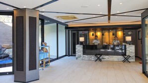 Una moderna zona de recepción con mostrador de mármol, una recepcionista y una puerta de cristal que da a un patio con pared de piedra y una pequeña fuente.