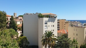 A coastal cityscape with a prominent white building featuring balconies and a red-tiled roof.