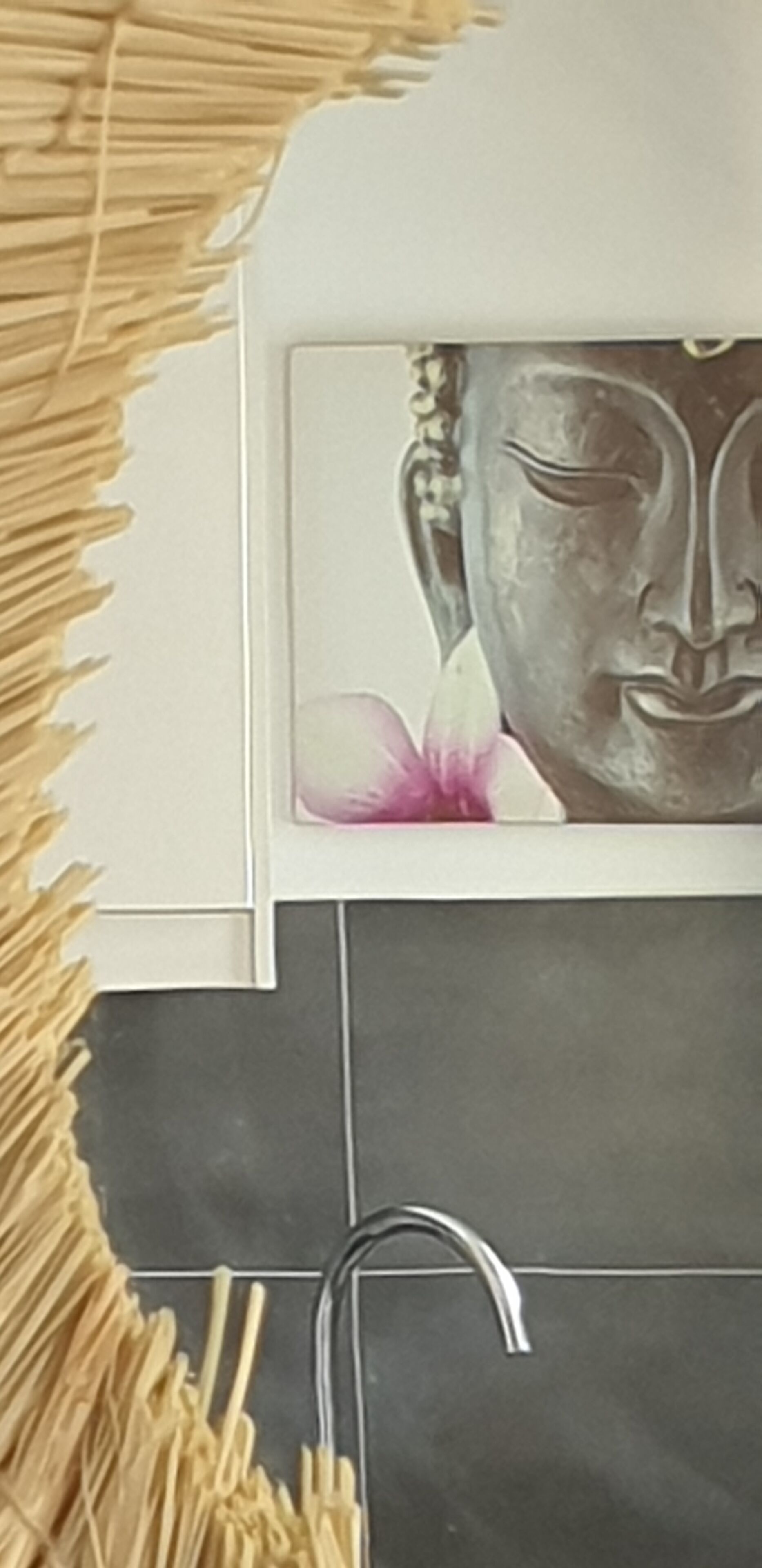 A bathroom with a tiled wall, a faucet, and a framed picture of a Buddha statue with a pink flower.
