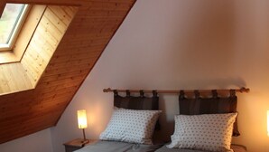 Een kamer met een schuine plafond, dakraam, een bed met twee kussens en bedlampjes.