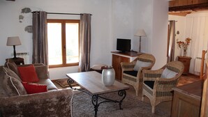 Een gezellige woonkamer met een bank, twee rieten stoelen, een salontafel en een televisie.