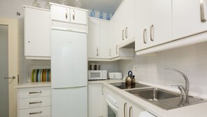 Cozinha moderna com armários brancos, micro-ondas embutido, chaleira e pia de aço inoxidável.