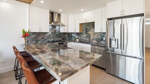 A modern kitchen with a marble countertop, stainless steel appliances, and white cabinetry.