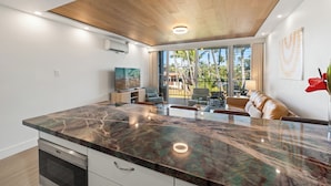 A modern kitchen with a marble countertop, built-in appliances, and a large window overlooking a balcony with outdoor furniture.