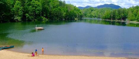 A lake surrounded by forest with a sandy beach and a dock.