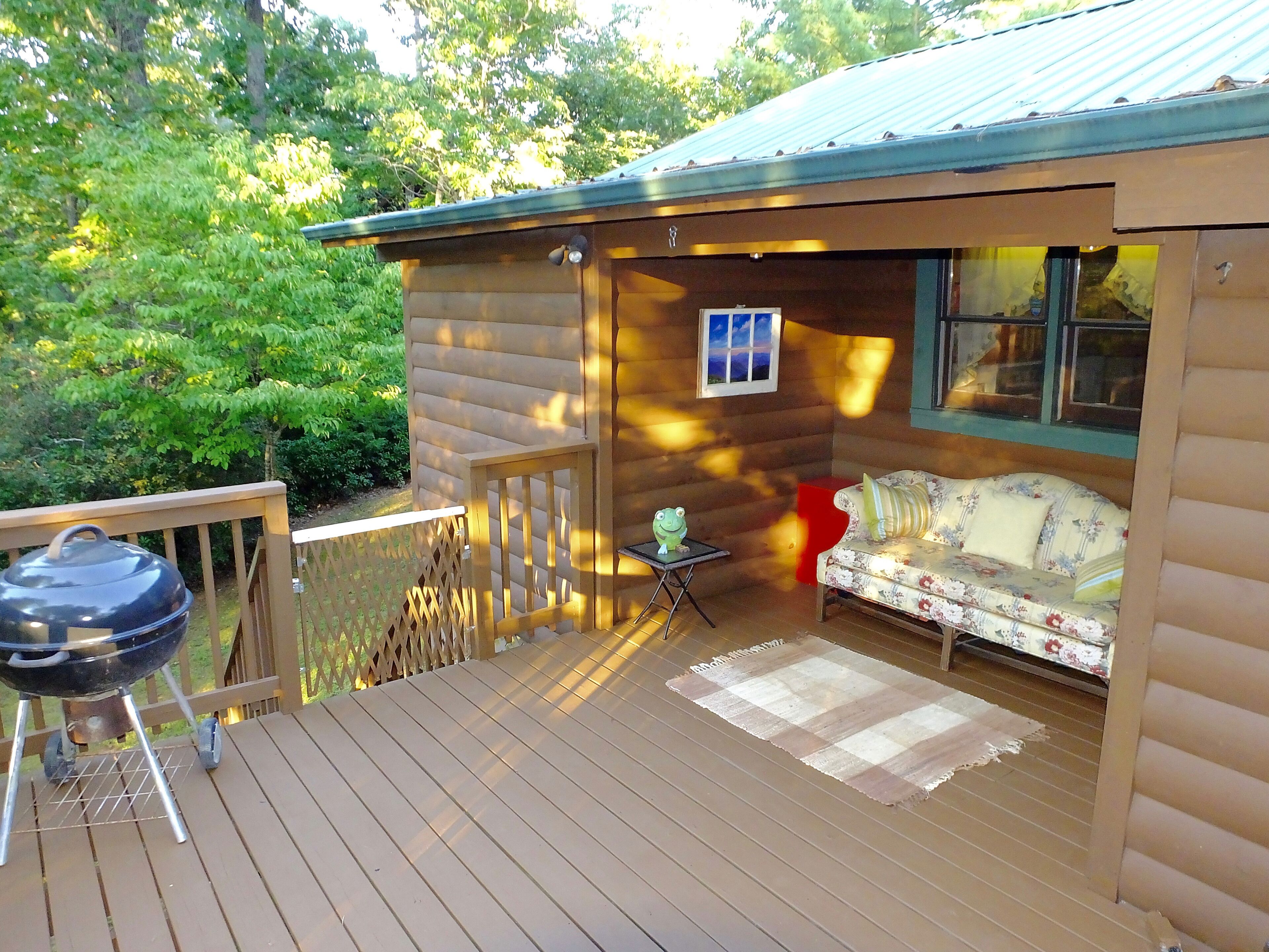 A wooden deck with a grill, a sofa, and a small table with a frog figurine.