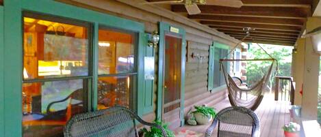 A covered porch with wicker furniture, a hammock, and potted plants.