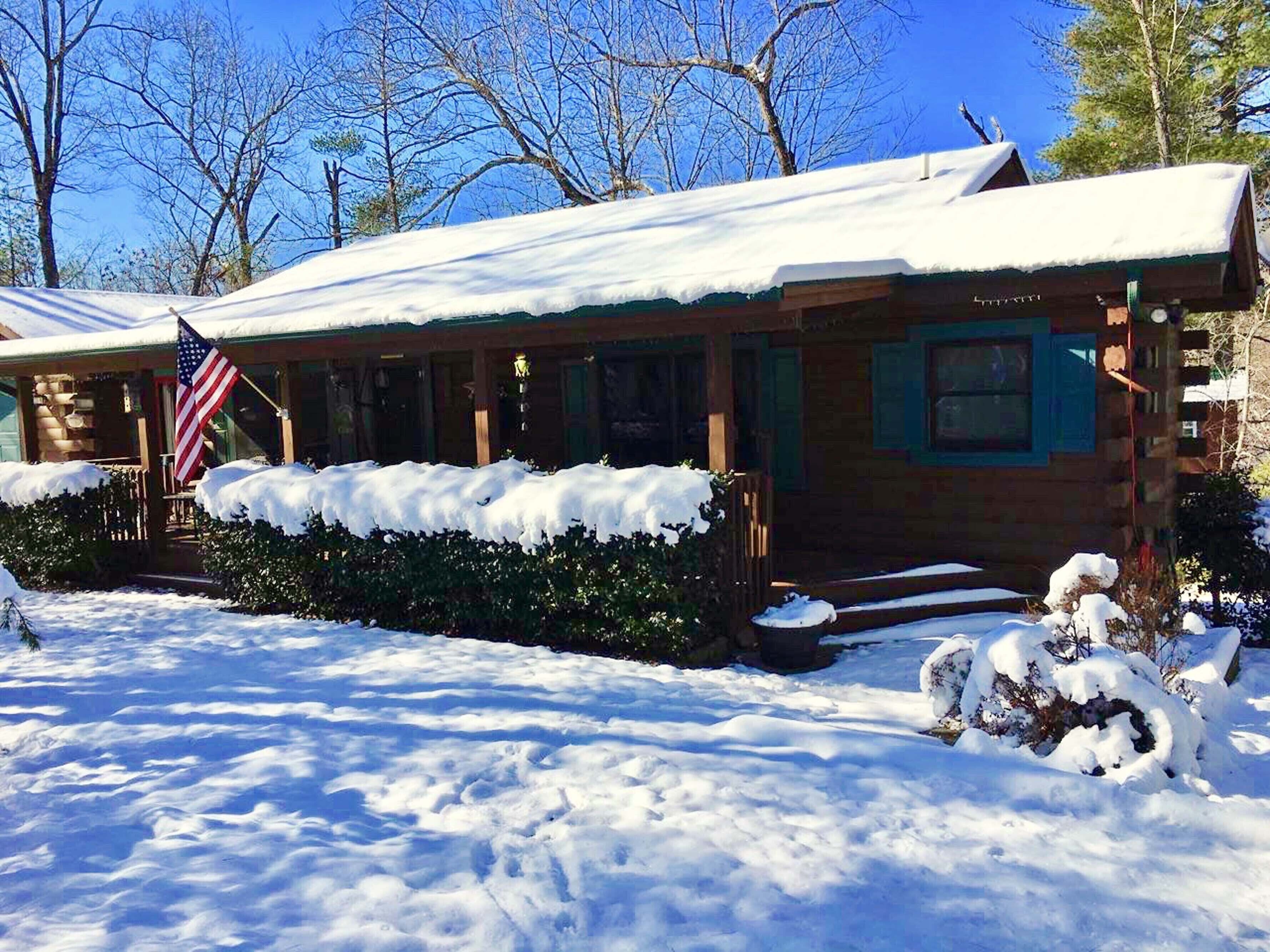 A log cabin with a snow-covered roof and a porch.