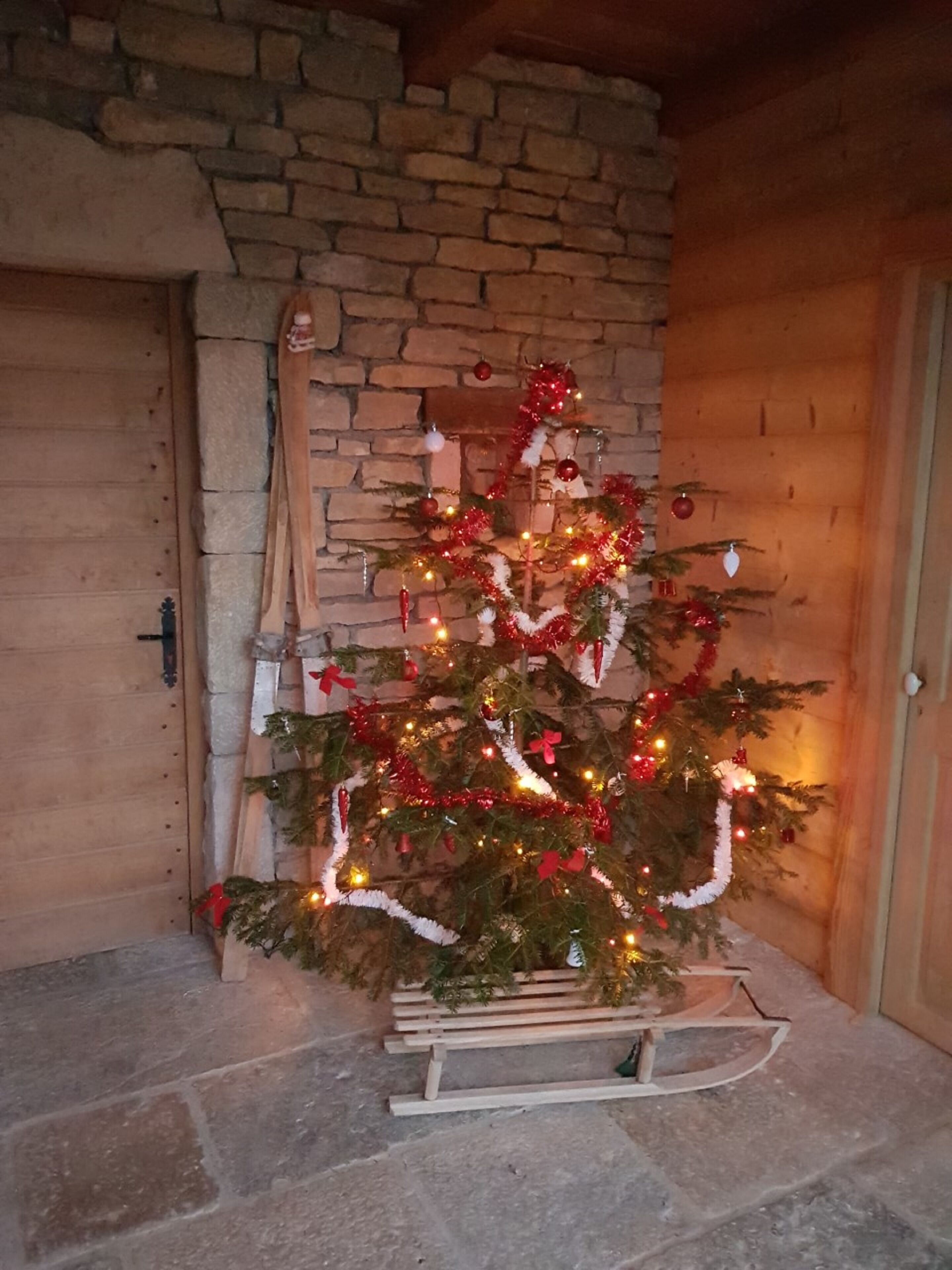 A decorated Christmas tree in a rustic room with stone walls and wooden beams.