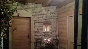 Una habitación con paredes de piedra, una puerta de madera, una pequeña mesa con sillas y una vela encendida.
