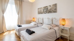 Een hotelkamer met twee bedden, een groot raam met gordijnen, een Boeddha-schilderij en bedlampjes.