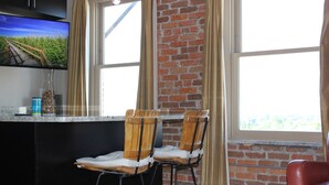 A kitchen with a brick wall, two wooden chairs, a TV, and a window with curtains.