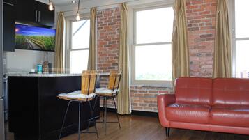 A modern kitchen with a large island, two bar stools, a red leather sofa, and a brick wall.