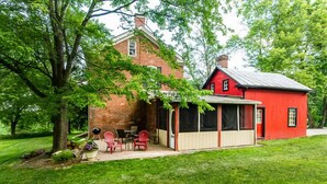 A brick house with a red exterior and a covered patio area with red chairs and a table.