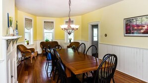 A dining room with a wooden table and chairs, a chandelier, and a painting on the wall.