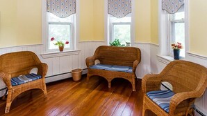 A room with three wicker chairs, a wooden floor, and windows with decorative valances.