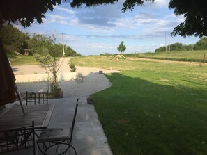 A patio area with a table and chairs, a gravel path leading to a grassy field, and a tree providing shade. - Pretty cottage in the countryside in a mas in Provence (Lurs)