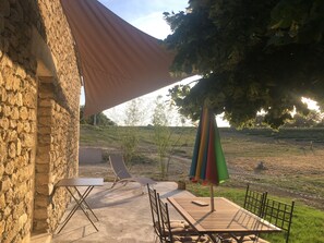 A patio with a table and chairs, a stone wall, and a large umbrella providing shade. - Pretty cottage in the countryside in a mas in Provence (Lurs)