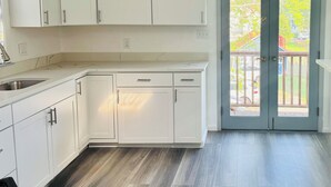 A modern kitchen with white cabinets, a built-in oven, and a large window with a view of a garden.