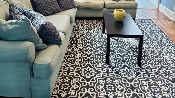 A living room with a sectional sofa, a patterned rug, a chandelier, and a 'BEACH' sign on the wall.