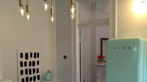 A kitchen with a teal refrigerator, a marble countertop, a wall-mounted light fixture, and a small table with a lamp.