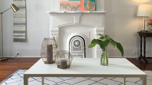 A room with a white fireplace, a table with decorative items, and wall art.
