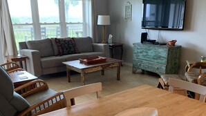 Una sala de estar con una mesa de comedor de madera, un sofá, un televisor y vistas al balcón.