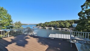 A wooden deck with a white railing overlooking a marina with boats and a forested shoreline.