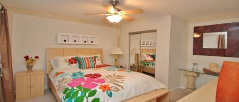 A bedroom with a bed, a ceiling fan, a bedside table, a mirror, and a small cabinet.