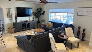 A living room with a sectional sofa, a television, a ceiling fan, and a large window with blinds. - Lake House to RELAX and Have FUN!!  FREE Wi-Fi. (Lake Havasu City)