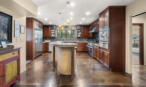 A spacious kitchen with wooden cabinets, a central island, stainless steel appliances, and pendant lighting.