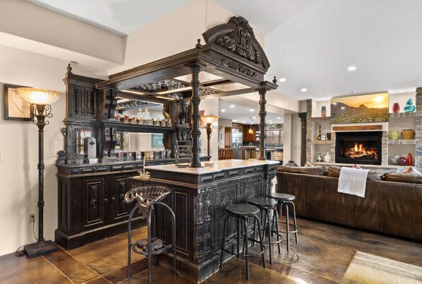 A bar area with a dark wood bar, stools, and a fireplace.