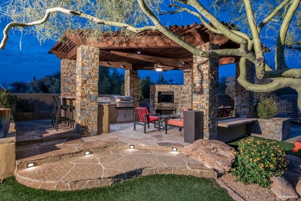 An outdoor patio with stone flooring, a grill, and seating under a pergola.