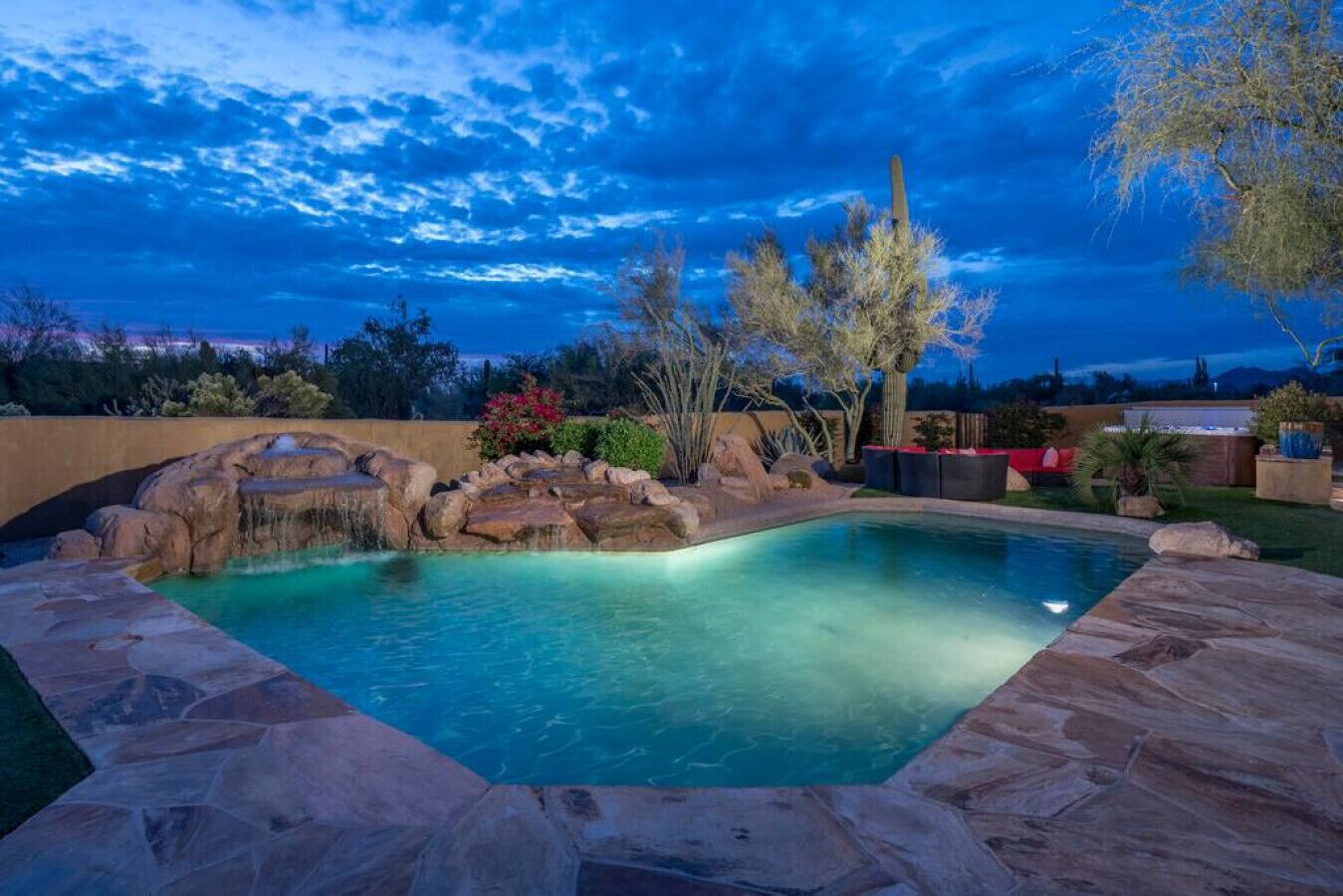 A swimming pool with a waterfall feature, surrounded by rocks and plants.