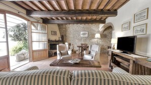 A cozy living room with a stone wall, wooden beams, a fireplace, a television, and striped sofas. - Tuscan Apart for 4/5 persons, WIFI, AIR-CO, SW-POOL, all comforts in the country (Montespertoli)