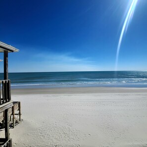 Ein Strand mit einer Holzkonstruktion, vermutlich einer Rettungswache, und einem wolkenlosen, blauen Himmel.