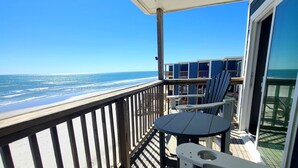 A balcony with a view of the ocean, wooden deck, and outdoor furniture.