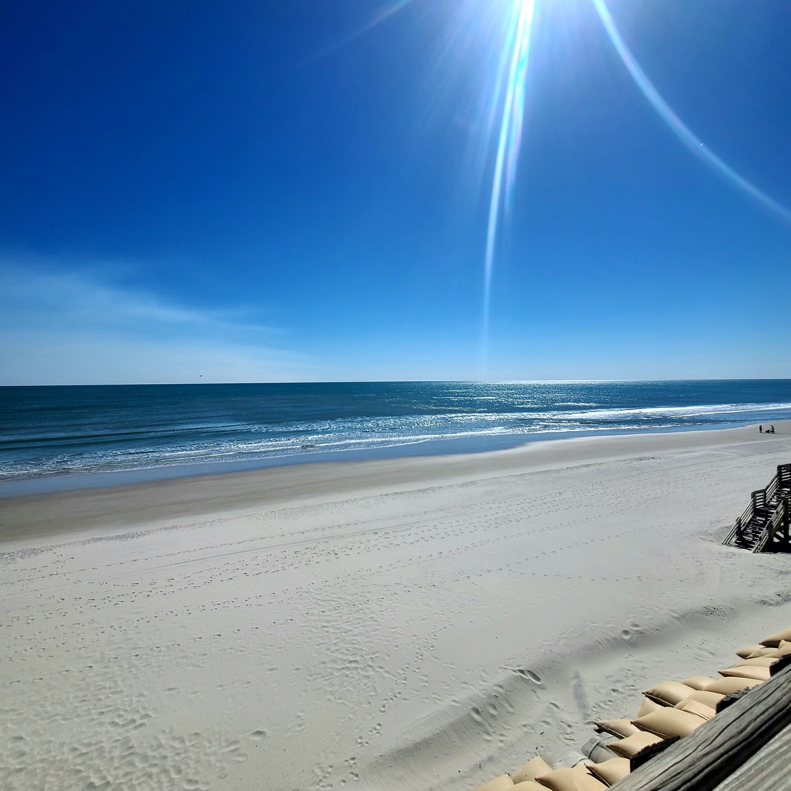 Una playa con cielo despejado, mar tranquilo y huellas en la arena.