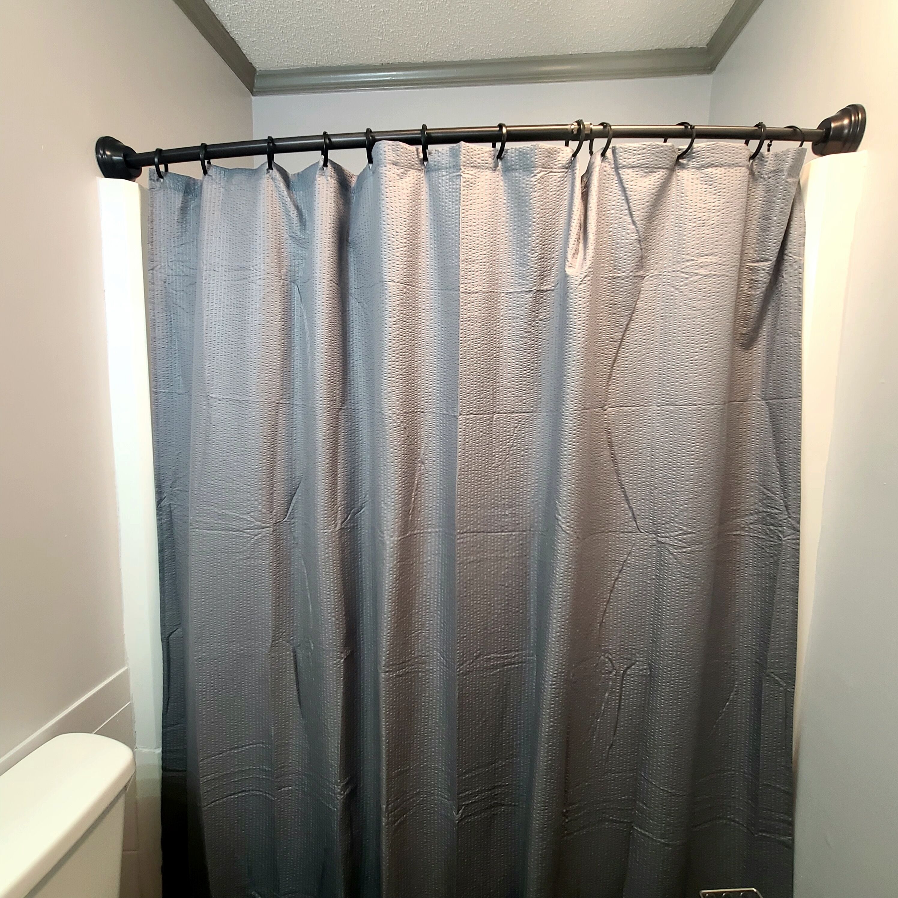 A bathroom with a shower curtain, a toilet, and a ceiling with a textured finish.